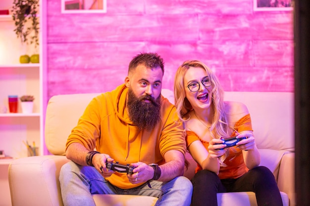 Belle fille blonde souriante en jouant à des jeux vidéo avec son petit ami à l'aide de contrôleurs sans fil sur un téléviseur grand écran