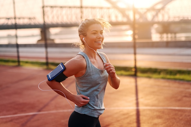 Belle fille blonde sportive fit écouter de la musique et courir tôt le matin à l'extérieur.