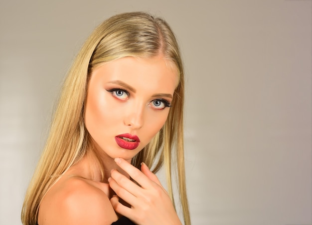 Belle fille blonde touchant son visage. Fille assez sexy, jolie femme aux cheveux longs, lèvres rouges, maquillage professionnel, peau parfaite. Modèle attrayant élégant avec un beau visage. Beauté, spa. Espace de copie