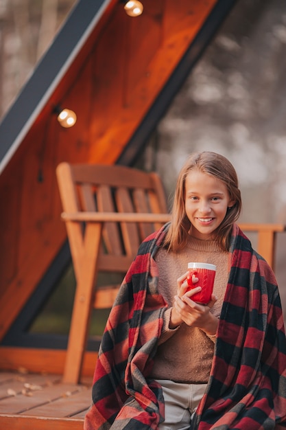 Belle fille avec une boisson chaude profitant de la journée d'automne sur la terrasse