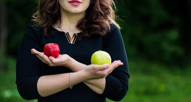 Belle fille bouclée dans une robe noire tenant une pomme verte dans la forêt