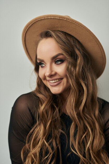 belle fille avec des boucles se tient au mur dans un body et un chapeau