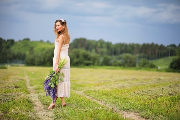 Belle fille avec un bouquet de fleurs bleues sur la nature en été