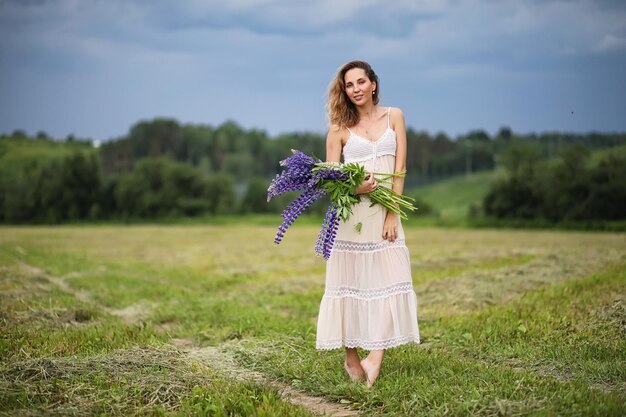 Belle fille avec un bouquet de fleurs bleues sur la nature en été