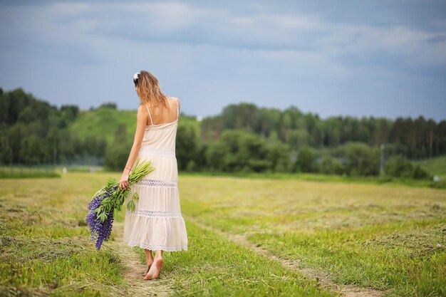 Belle fille avec un bouquet de fleurs bleues sur la nature en été