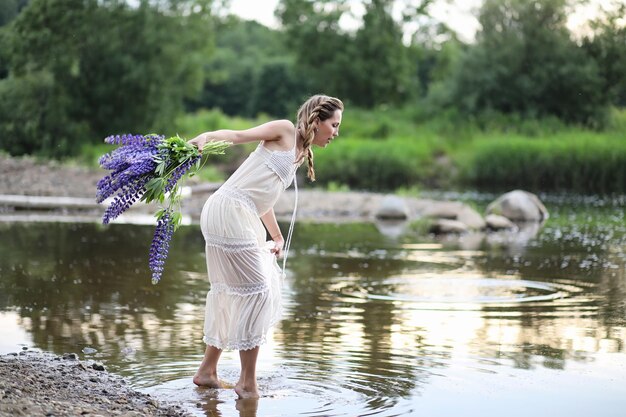 Belle fille avec un bouquet de fleurs bleues sur la nature en été