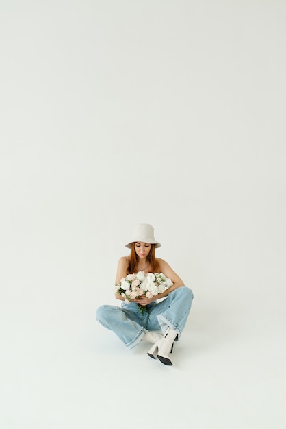 Belle fille avec un bouquet de fleurs dans un chapeau et un jean bleu