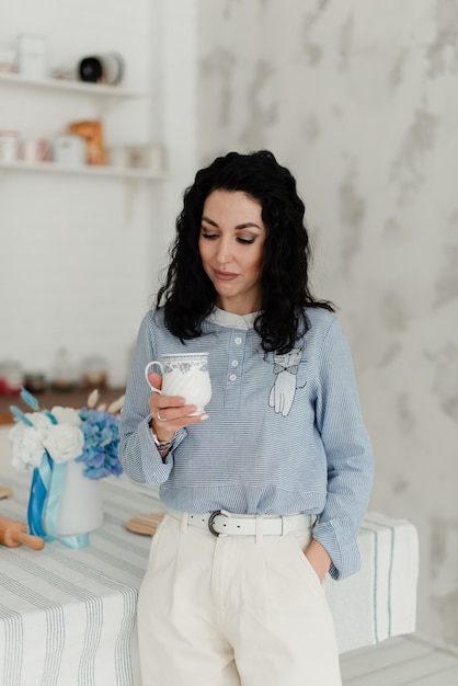 Belle fille brune aux cheveux ondulés noirs tenant une tasse dans ses mains