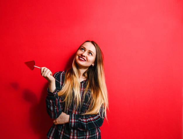 Une belle fille brune avec un bonbon à la main s'amusant sur un fond rouge.