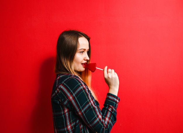 Une belle fille brune avec un bonbon à la main s'amusant sur un fond rouge.