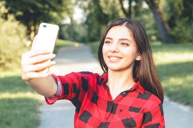 belle fille brune dans une chemise à carreaux rouge prenant selfie