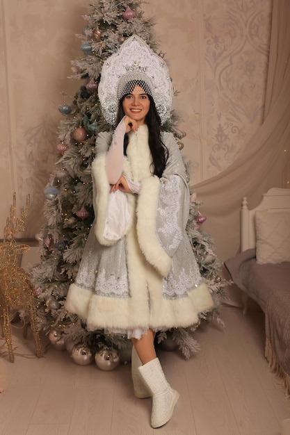 une belle fille brune dans un costume de jeune fille des neiges se tient à l'arbre de Noël