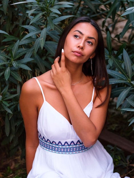 Belle fille brune dans une robe blanche se trouve à proximité d&#39;un arbre vert