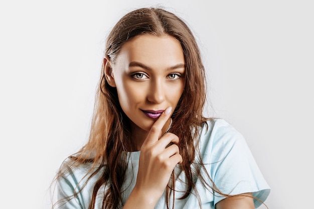 Belle fille brune douce aux cheveux longs avec du maquillage de mode avec des lèvres violettes sur une surface grise isolée