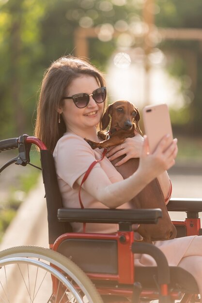 belle fille brune en fauteuil roulant en été lors d'une promenade avec un mignon chien teckel prend un se