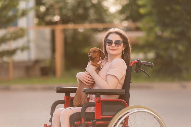 belle fille brune en fauteuil roulant en été lors d'une promenade avec un mignon chien teckel