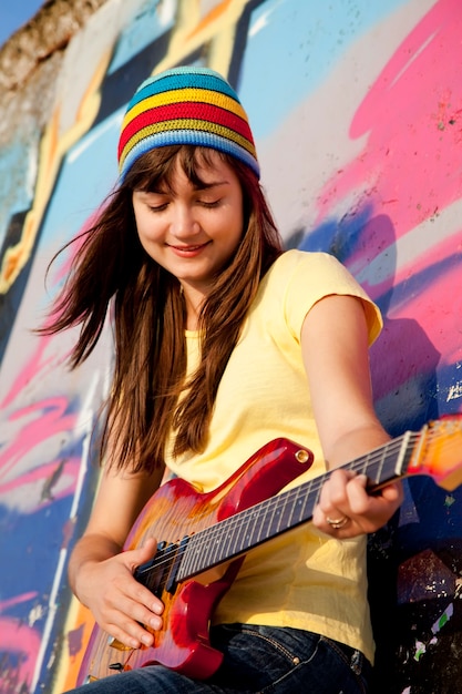 Belle fille brune avec guitare et mur de graffitis