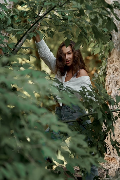 belle fille brune en jeans et une chemise blanche posant sur les ruines de la forêt