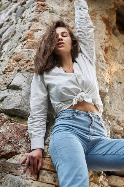 belle fille brune en jeans et une chemise blanche posant sur les ruines de la forêt