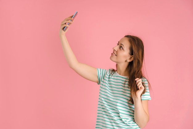 Belle fille brune prend un selfie sur fond rose