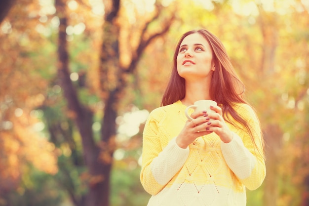 Belle fille brune avec une tasse dans le parc.