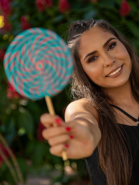 Belle fille brune tenant une sucette colorée dans la forêt. Mise au point sélective.