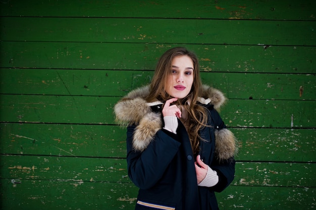 Belle fille brune en vêtements chauds d'hiver. Modèle sur veste d'hiver sur fond de bois vert.