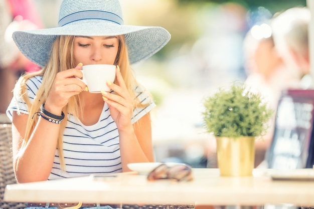 Belle fille buvant du café dans une terrasse de café. Jeune femme de portrait d'été.