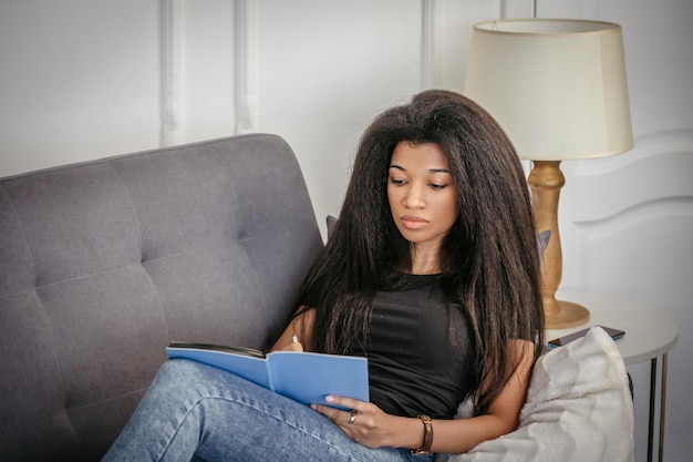 Photo une belle fille avec un cahier est assise sur le canapé et prend des notes dans un cahier