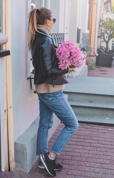 Une belle fille caucasienne aux cheveux blonds dans un manteau gris et un jean bleu avec un bouquet de rose