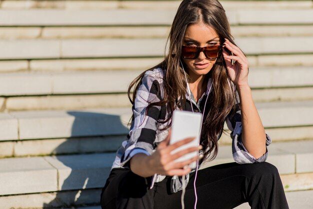 Belle fille caucasienne brune écoutant de la musique avec un casque dans les escaliers dans la ville