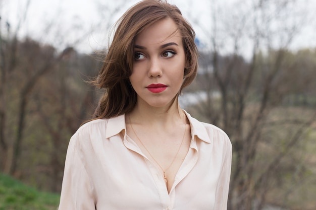 Belle fille caucasienne avec des lèvres rouges, des cheveux bouclés dans un chemisier beige élégant semble pensif à part. Concept de solitude