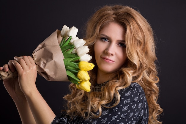 Belle fille caucasienne qui pose en studio sur fond isolé noir avec bouquet de fleurs