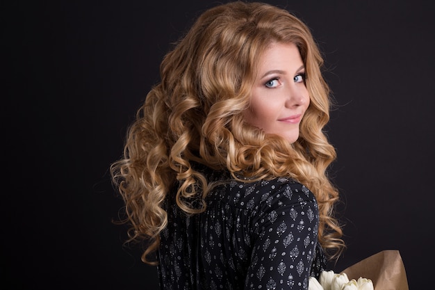 Belle fille caucasienne qui pose en studio sur fond isolé noir avec bouquet de fleurs