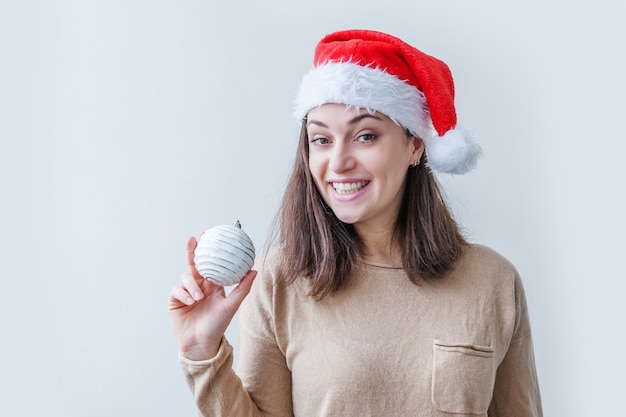 Belle fille en chapeau de père Noël rouge tenant boule d'ornement d'arbre de Noël dans la main