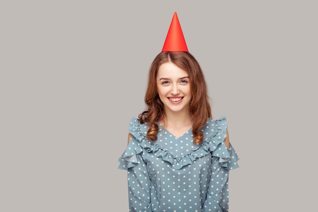 Belle fille en chemisier à volants et chapeau de fête drôle regardant la caméra, souriant en profitant de l'anniversaire