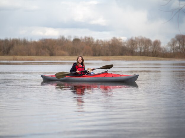 Une belle fille et un chiot Jack Russell Terrier voyagent sur un kayak rouge.