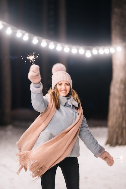 Photo belle fille avec des cierges magiques dans les mains joyeux hiver dans la forêt guirlande lumineuse festive