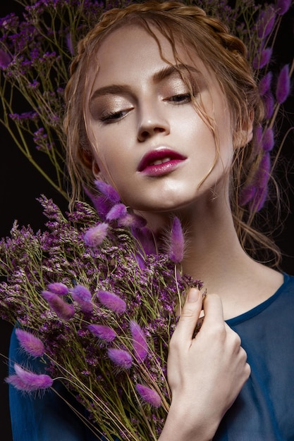 Belle fille avec une coiffure de maquillage doux sous la forme de tresses fleurs sèches robe bleue