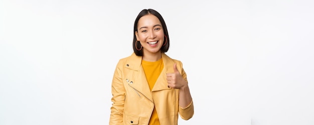 Belle fille coréenne souriante montrant les pouces vers le haut comme un geste recommandant un magasin ou une entreprise debout satisfaite sur fond blanc