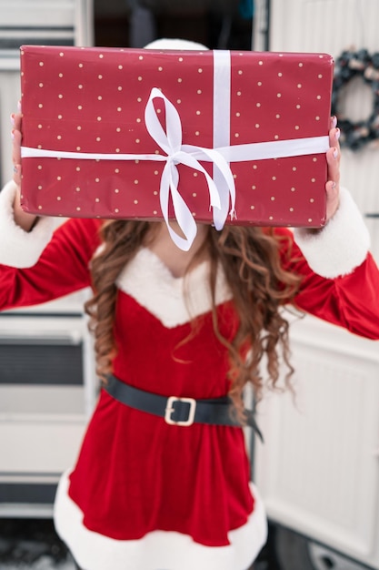 Belle fille en costume de père noël avec boîte-cadeau au camping d'hiver se prépare pour le nouvel an nouvel an