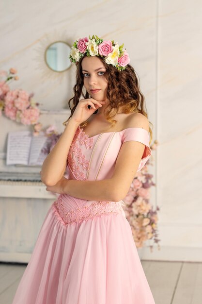 Une belle fille avec une couronne de fleurs sur la tête et une longue robe rose est photographiée dans un studio photo Spring PHOTOSESSION