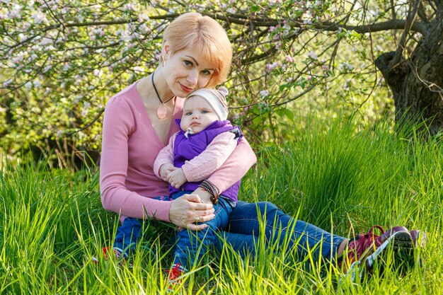 Une belle fille dans les bras d'une enfant dans un parc en fleur en gros plan