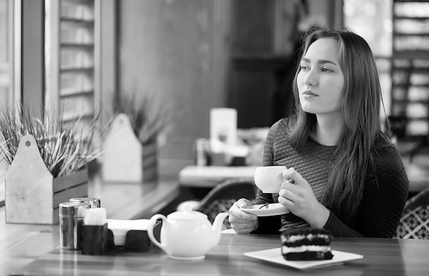 Belle fille dans un café assis et buvant du thé avec un dessert