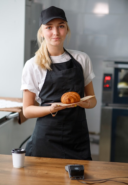 Belle fille dans un café et une boulangerie tenant un croissant