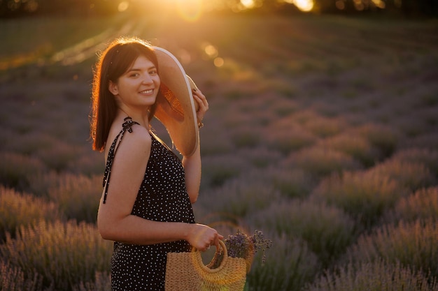 Belle fille dans un champ de lavande avec un chapeau de paille et un sac en osier dans ses mains