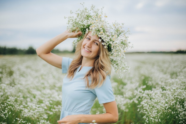 belle fille dans un champ de marguerites. fille dans un chapeau de paille et une robe bleue. champ de camomille en été