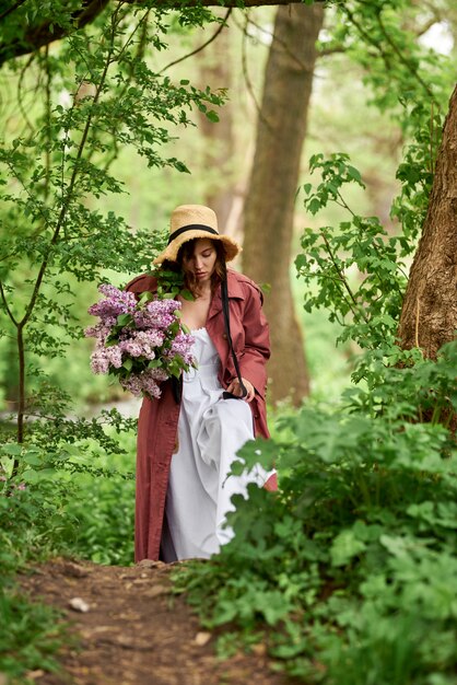 Belle fille dans un chapeau de paille dans la forêt Fille avec des fleurs lilas au printemps