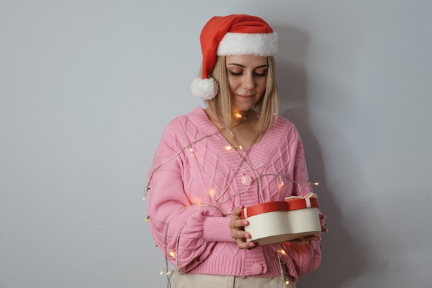 Belle Fille Dans Un Chapeau De Père Noël, Décorée De Lanternes Du Nouvel An Avec Un Cadeau Dans Ses Mains, Gros Plan. Le Concept De Noël Et Du Nouvel An.