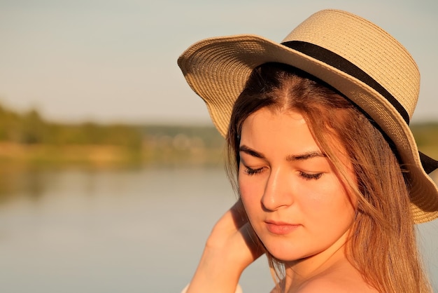 Une belle fille dans un chapeau se tient sur le rivage chapeau à la main